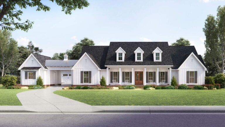 A front view of a modern farmhouse-style home with a bright and welcoming design. The exterior features white board and batten siding, a dark shingled roof, and a metal roof over a portion of the attached garage. The house has a large, covered front porch supported by white columns, leading to a wooden front door with glass panels. The porch is adorned with a pair of rocking chairs, adding to the home’s charm. Above the porch, there are three dormer windows that enhance the roofline. The front yard is spacious and landscaped with a well-manicured lawn, shrubs, and small trees, all set against a backdrop of mature greenery under a clear, sunny sky.